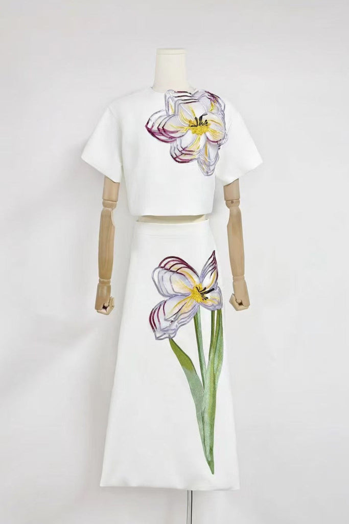Mannequin wearing a white outfit with floral designs on a plain background